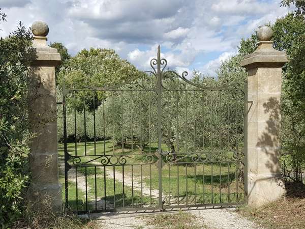 L'allée de cette propriété a été cloturée avec un portail à volutes en fer forgé et des piliers en pierre naturelle finition ancienne.