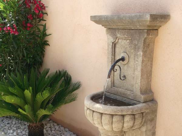 Point d'eau adossé contre un mur de maison avec cette fontaine en pierre à grodrons sculptés sur la vasque.