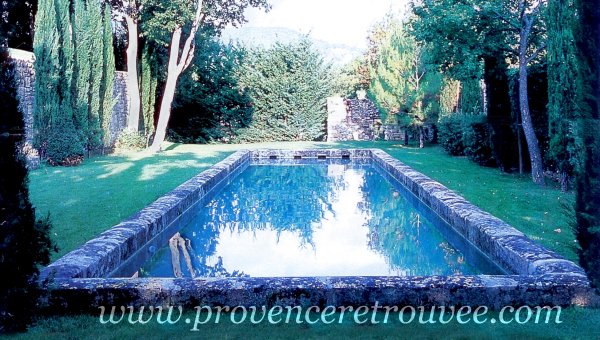 Dans un magnifique jardin, piscine ayant l'aspect d'un vieux bassin ancien grâce à sa margelle réalisée avec des bordures anciennes en pierre